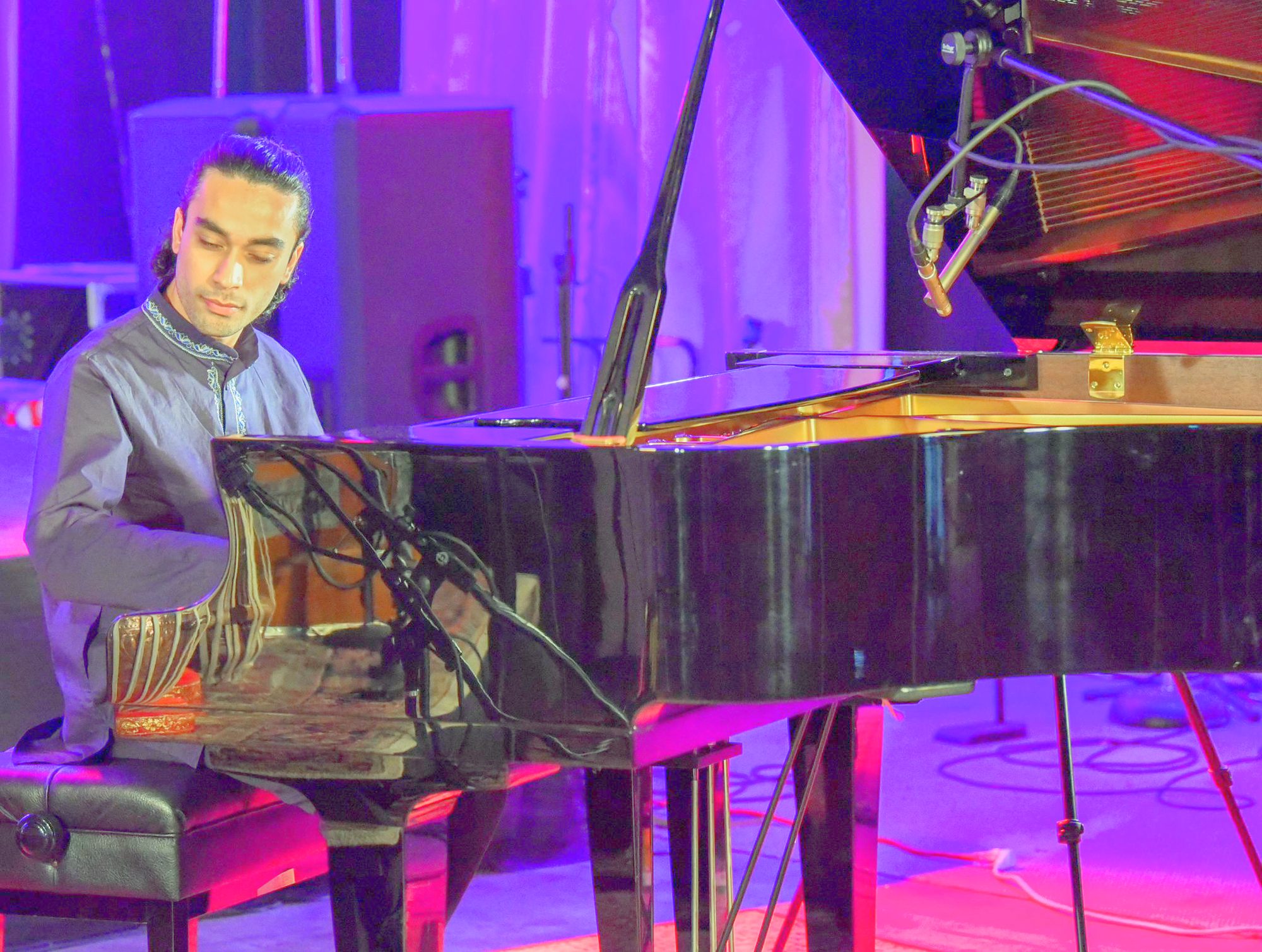 Elham Fanoos performing at a grand piano under stage lighting