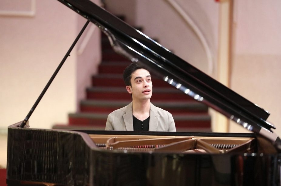 Elham Fanoos at a grand piano, lid raised, before a red-carpeted staircase